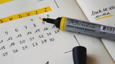 Yellow marker on a planner next to a calendar showing dates with notes.