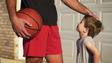 Adult holding a basketball affectionately pats a child's head.