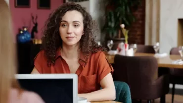 Person in a red shirt sitting at a restaurant table, talking to someone