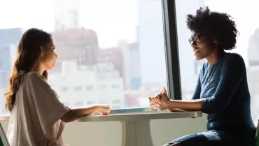 Two people talking at a table in a brightly lit room.