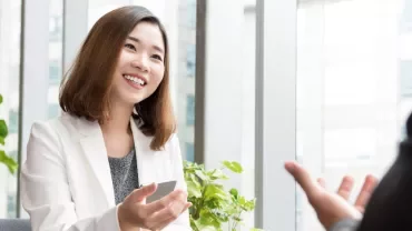 一位穿著白色西裝的人在辦公室微笑，前面有植物。