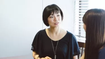 兩人坐在桌邊交談，一人看向另一人。