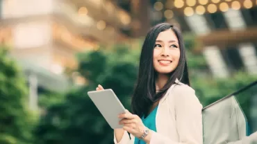 Person smiling while holding a tablet, cityscape in the background.