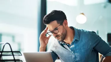 Person looking at a laptop screen with a thoughtful expression.