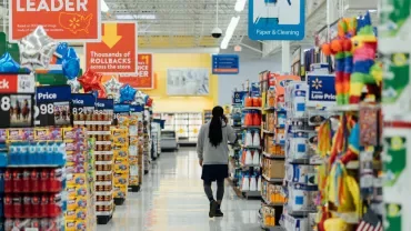 Customer walking down a grocery store aisle with shelves full of products.