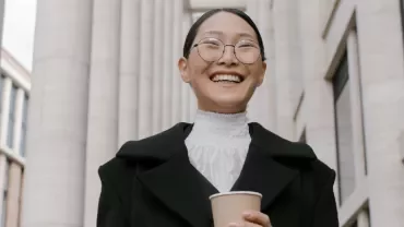Person smiling outdoors, holding a coffee cup, with columns in the background.