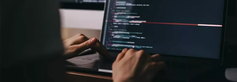 Hands typing code on a laptop in a dark room
