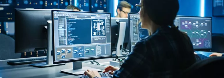 Person working at a desk with computer screens displaying code and diagrams.