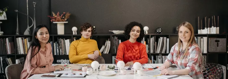 A group of people smiling at a conference table, with a bookshelf in the background.