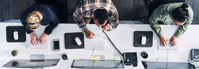 Overhead view of three people working at computers in an office.