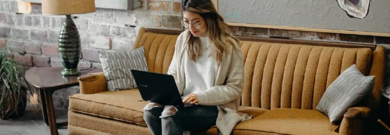Person sitting on a vintage sofa using a laptop in a cozy room.