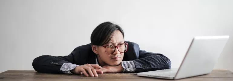 A person leaning on a desk, looking at a laptop.