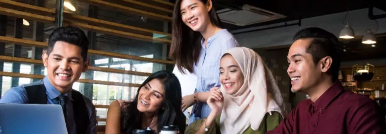 Five friends smiling while looking at a laptop in a café.