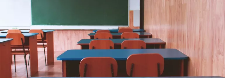 An empty classroom with arranged desks and a green chalkboard