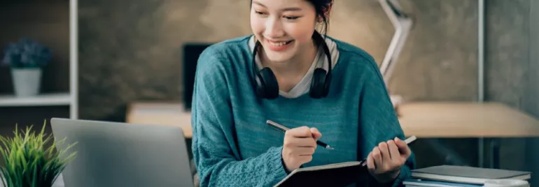 An adult using a laptop and notebook at a desk.