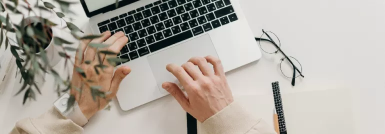 Person typing on a laptop with glasses and notebook nearby