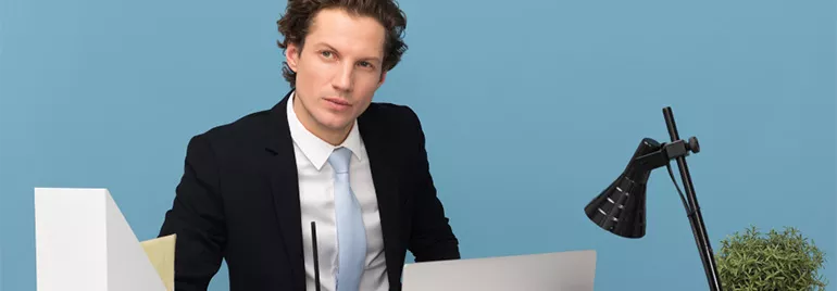 Professional sitting at a desk with a laptop and lamp.
