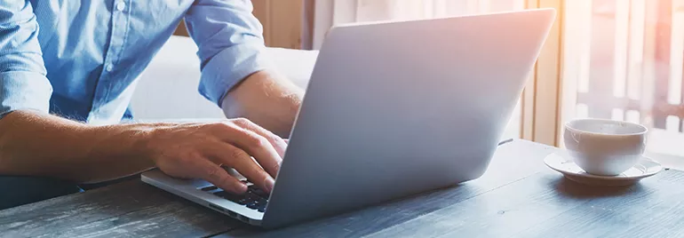 Person typing on a laptop with a cup of coffee on the table.