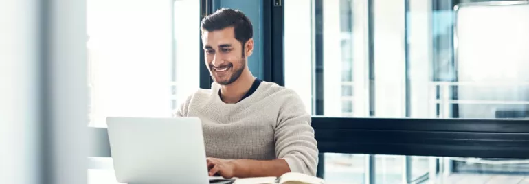 A person smiling while looking at a laptop on a table.