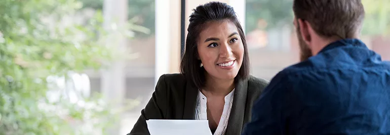 Two people having a conversation in an office with papers.