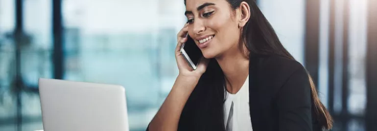 Person smiling while talking on phone and using laptop.