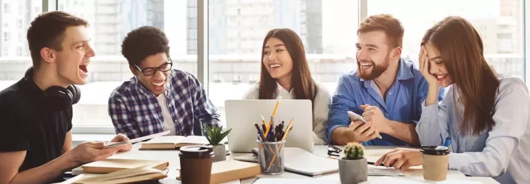 Group of students laughing and working together around a table.