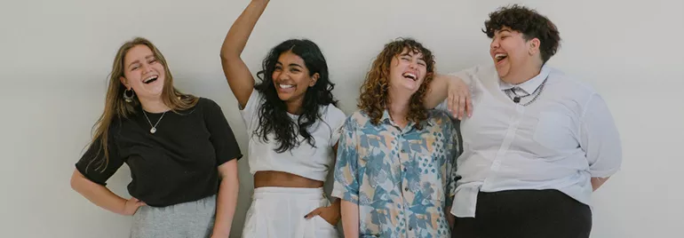 Four people standing together, smiling in front of a white background.