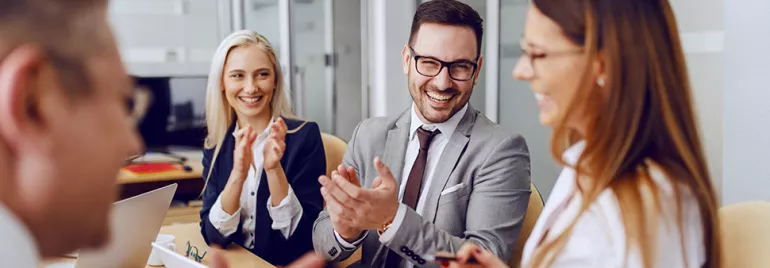 Colleagues having a cheerful discussion and clapping in a meeting.