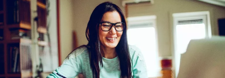 Person smiling while using a computer in a room with bookshelves.