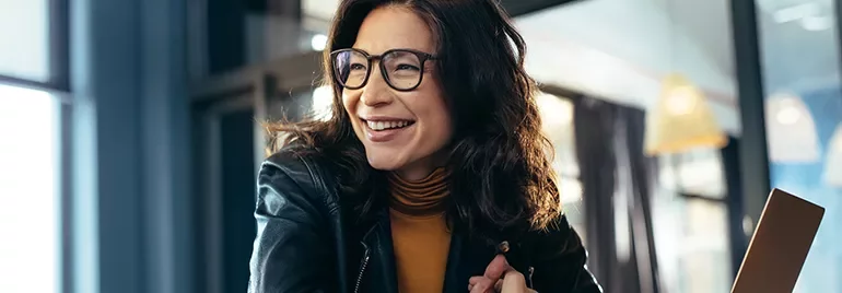 A person wearing glasses smiling while seated in a cafe.