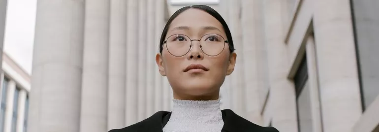A person wearing formal attire and glasses walks between tall buildings.