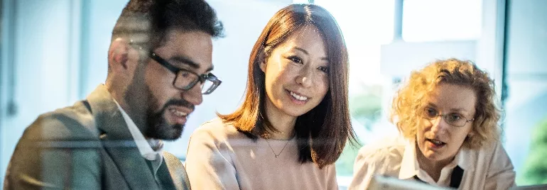 Three people looking at a computer screen in an office setting.