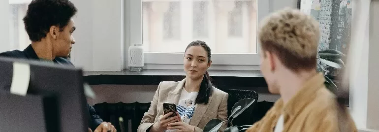 Three people having a conversation in an office setting, one holding a phone.