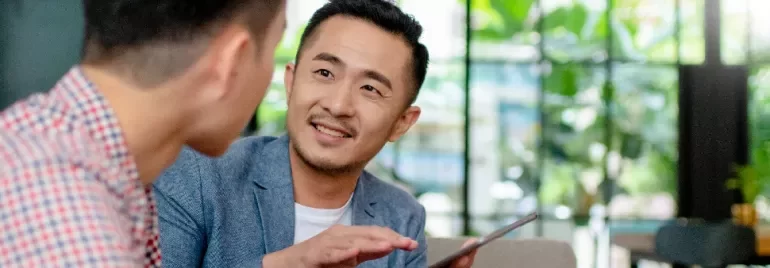 One male professional holding a tablet and in discussion with another male professional