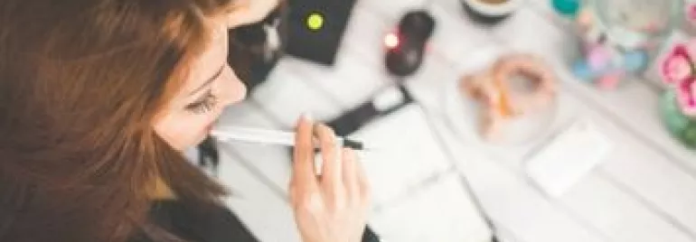 女子正在桌上筆記本旁思考，周圍有咖啡和甜甜圈。