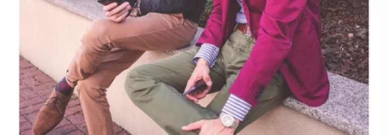 兩個人坐在戶外長椅上，手裡拿著手機。