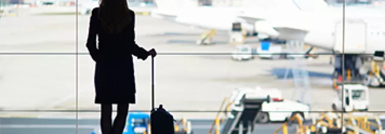 一名旅客在機場窗前等待，旁邊放著行李箱。