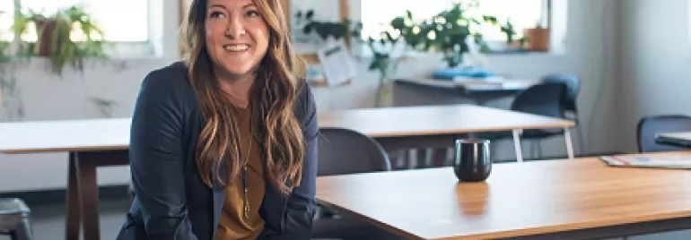 Person smiling while sitting at a desk in an office with plants.