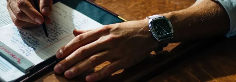 A hand wearing a watch writing on a notepad.