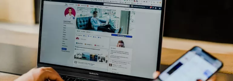 Laptop open to a social media profile next to a hand holding a smartphone.
