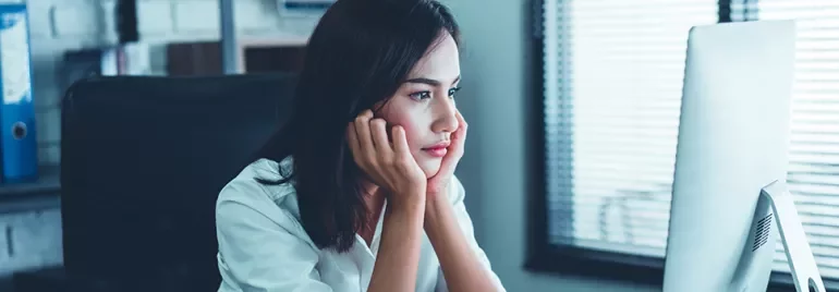 Person sitting at a desk looking thoughtfully at a computer screen.