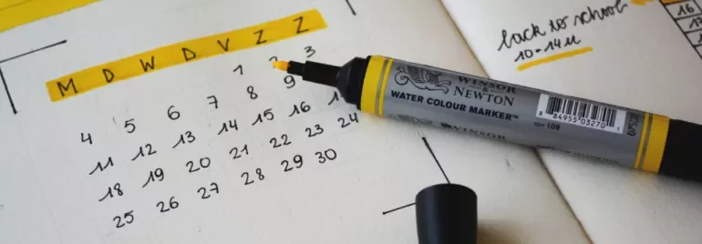 Yellow marker on a planner next to a calendar showing dates with notes.