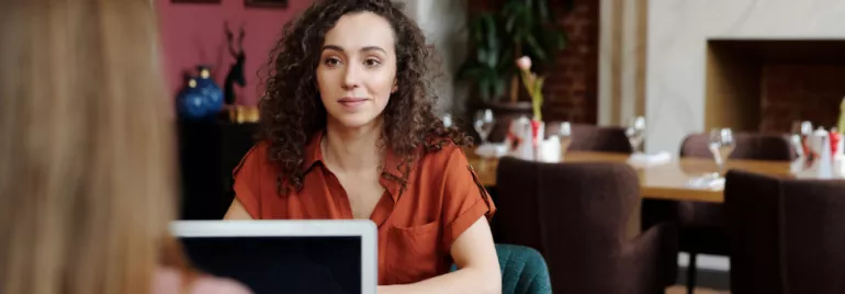 Person in a red shirt sitting at a restaurant table, talking to someone