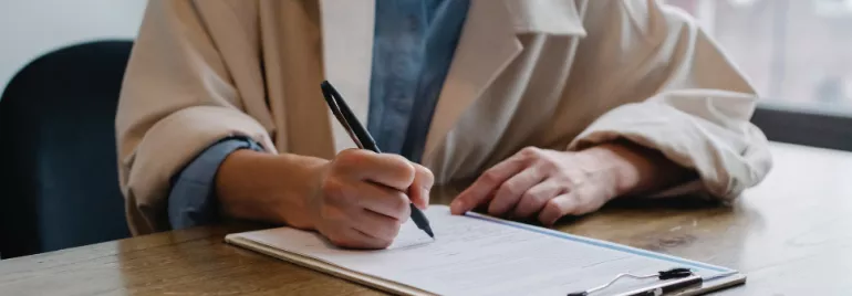 Person writing on a document at a desk.