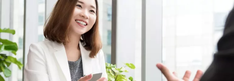 一位穿著白色西裝的人在辦公室微笑，前面有植物。