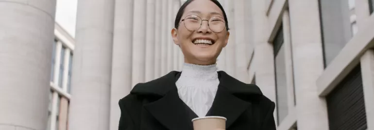 Person smiling outdoors, holding a coffee cup, with columns in the background.