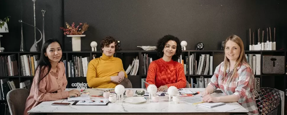 A group of people smiling at a conference table, with a bookshelf in the background.