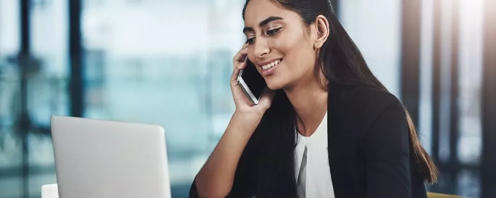 Person smiling while talking on phone and using laptop.
