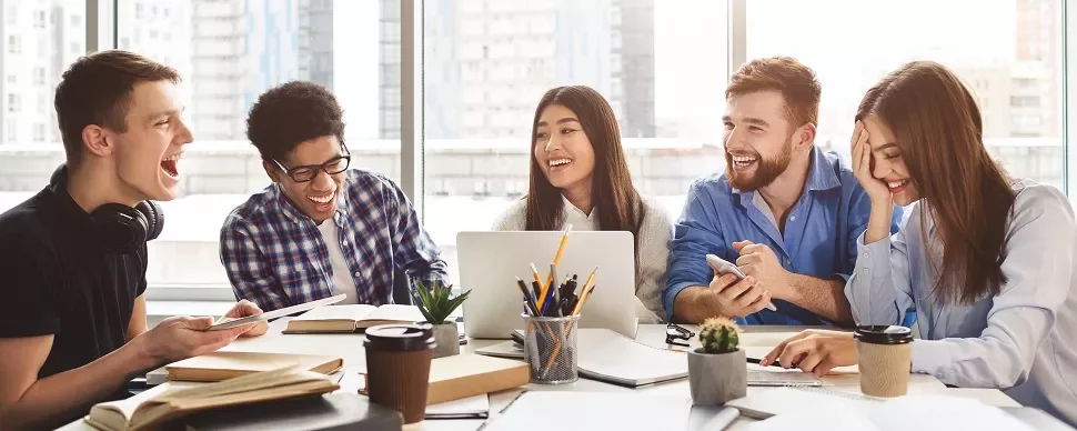 Group of students laughing and working together around a table.