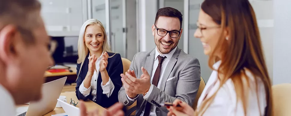 Colleagues having a cheerful discussion and clapping in a meeting.